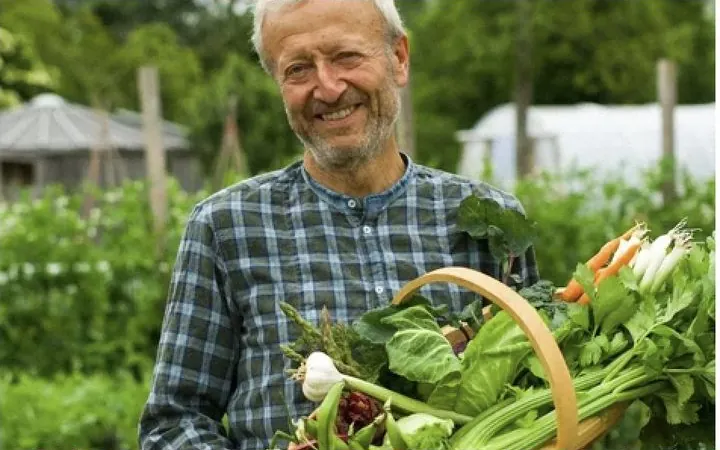 Charles Dowding holding a basket of fresh vegetables in his garden