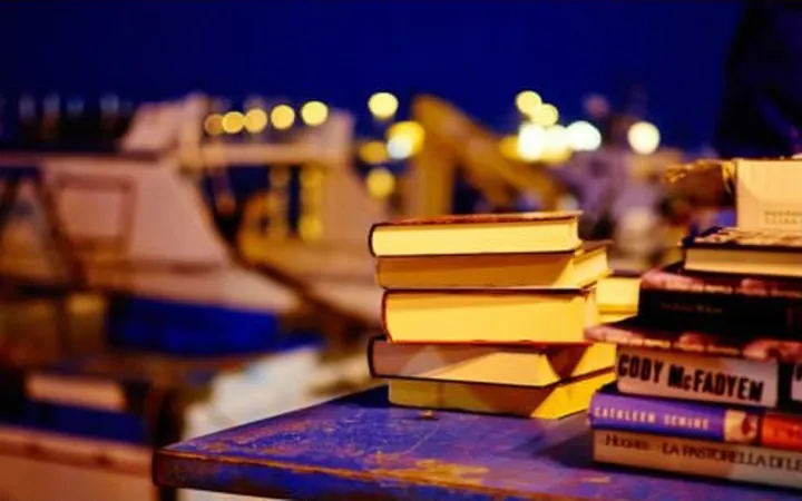 Stacks of books on a table by a harbor at night