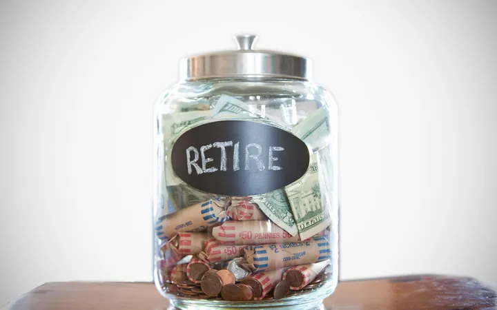 A glass jar labeled Retire, filled with cash and coin rolls