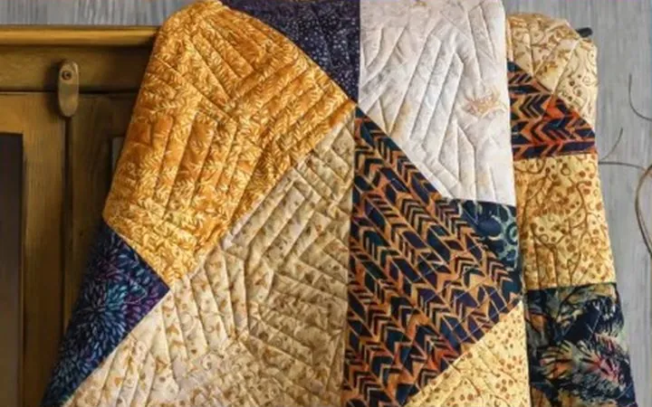 A finished patchwork quilt draped over a chair
