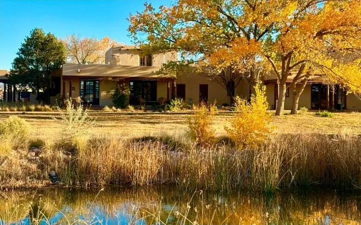 An adobe campus building behind autumn trees and a pond